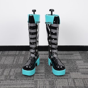 Może przedstawiać: Para czarnych butów na platformie z błyszczącym wykończeniem. Buty mają jasnoniebieską podeszwę i akcenty, ze srebrnymi paskami i ćwiekami. Buty mają wysoką cholewkę i unikalny design, idealne do cosplayu.