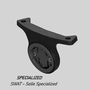 May include: A black Specialized SWAT bicycle computer mount. The mount has a curved design with two mounting holes and a circular area for the computer. The text "SPECIALIZED" and "SWAT - Selle Specialized" are printed at the bottom.
