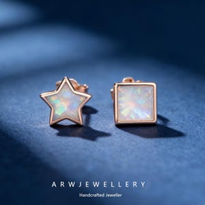 May include: A pair of rose gold earrings, one star-shaped and one square, each featuring an iridescent opal center. The earrings are set against a dark blue background. The text "ARW JEWELLERY" and "Handcrafted Jeweller" are at the bottom.