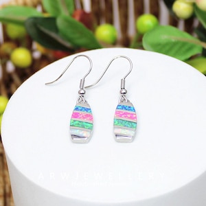 May include: A pair of silver earrings with a colorful, layered design. Each earring features a rectangular, opal-like stone with horizontal stripes of pink, blue, green, and white. The earrings have a simple hook closure.