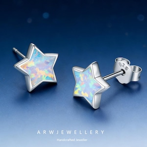May include: A pair of star-shaped stud earrings. Each earring features a silver-colored frame with an iridescent, opal-like center. The earrings are displayed on a blue background. The text "ARW JEWELLERY" and "Handcrafted Jeweller" are at the bottom.