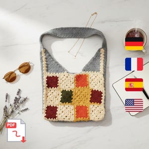May include: A handmade crochet shoulder bag with a patchwork design. The bag features a gray strap and a body composed of colorful squares in cream, red, orange, yellow, and green. Sunglasses and a necklace are also visible.