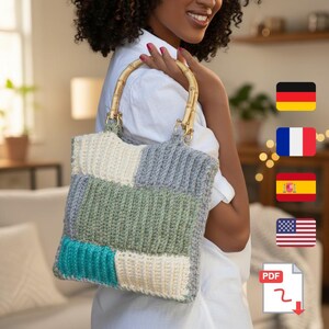 May include: A handmade crochet tote bag with a patchwork design. The bag features a bamboo handle and gold-colored hardware. The color palette includes cream, gray, green, and teal. The bag is a stylish accessory for carrying items.