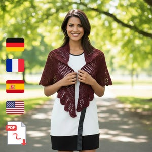 Peut inclure: Un châle en crochet bordeaux avec un bord festonné. Le motif ajouré est présenté sur une femme portant une robe blanche avec une bordure noire. L'arrière-plan est un cadre de parc vert flou.