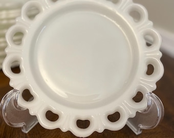 May include: A white, vintage-style plate with a scalloped edge featuring heart-shaped cutouts. The plate is displayed on a clear plastic stand, showcasing its delicate design. The plate has a glossy finish and is likely made of ceramic.
