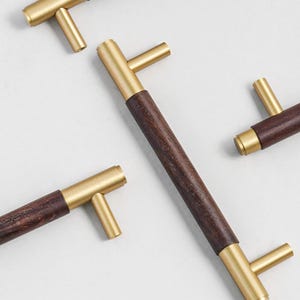 Peut inclure: Gros plan de plusieurs poign&eacute;es de meubles. Chaque poign&eacute;e pr&eacute;sente une poign&eacute;e en bois brun fonc&eacute; avec des accents m&eacute;talliques de couleur laiton. Les poign&eacute;es sont dispos&eacute;es &agrave; diff&eacute;rents angles sur un fond blanc.