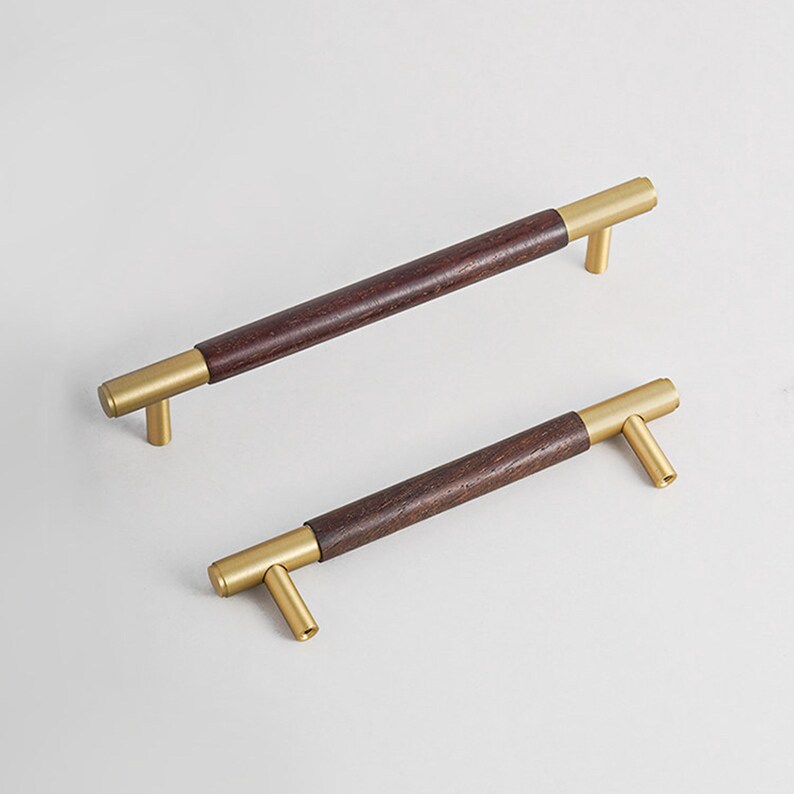 Peut inclure: Deux poign&eacute;es de meubles avec un centre en bois brun fonc&eacute; et des extr&eacute;mit&eacute;s en m&eacute;tal dor&eacute;. Les poign&eacute;es sont rectangulaires avec un design en forme de T &agrave; chaque extr&eacute;mit&eacute;. Fond blanc.