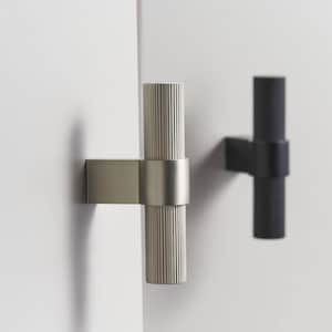 May include: Two modern cabinet pulls. One is silver-toned, the other is black. Each has a rectangular base and a cylindrical handle with vertical grooves. The handles are connected to the base with a circular band.
