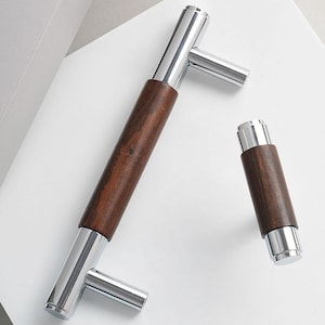 May include: Two pieces of hardware: a long handle and a smaller cylindrical piece. Both have a dark brown wooden center and polished silver-colored metal ends. The handle has a T-shaped design with a horizontal bar.