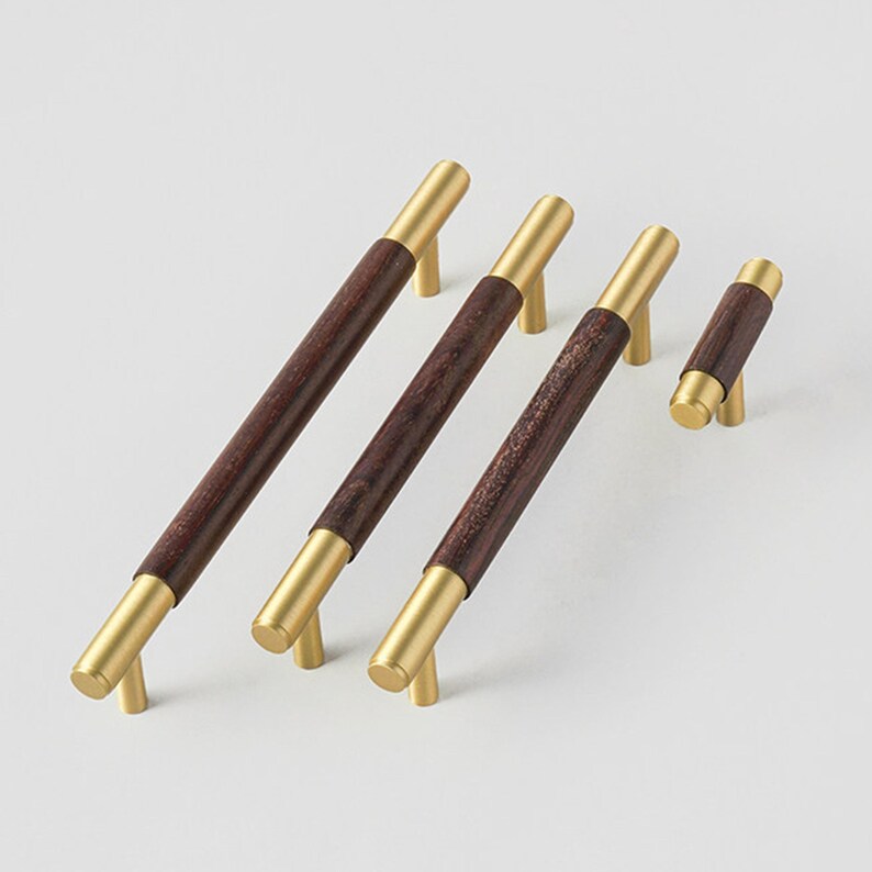 Peut inclure: Ensemble de quatre poign&eacute;es de meubles. Elles pr&eacute;sentent un centre en bois brun fonc&eacute; avec des extr&eacute;mit&eacute;s et des pieds en m&eacute;tal dor&eacute;. Les poign&eacute;es varient en taille, la plus longue mesurant environ 30 cm de long.