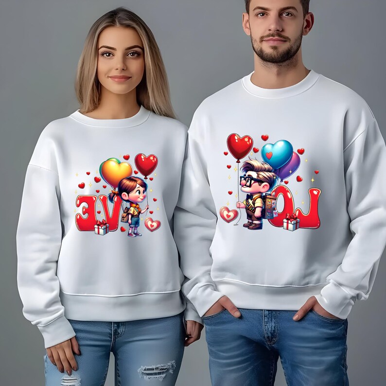 May include: White sweatshirts with matching cartoon graphics. One sweatshirt features a girl holding heart-shaped balloons next to the word "LOVE". The other sweatshirt has a boy with balloons next to the word "LOVE". Both sweatshirts have red heart accents.