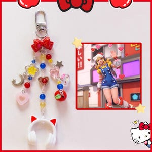 May include: A decorative keychain featuring a red bow, beads, and charms, including hearts, stars, and a headset. A cartoon image of a character in a blue outfit is in the background, along with Hello Kitty and apple graphics.