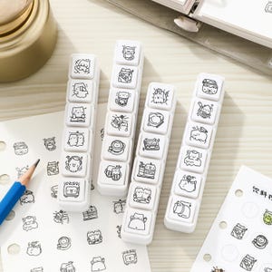 Pode incluir: Quatro blocos de carimbos retangulares brancos com ilustrações de linhas pretas de gatos de desenhos animados em várias atividades. Cada bloco contém seis carimbos quadrados individuais com designs únicos, incluindo gatos com leite, livros, fones de ouvido e comida.