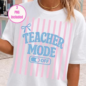 Puede incluir: Una camiseta blanca de manga corta con un patrón de rayas verticales de color rosa claro. El gráfico central muestra el texto "TEACHER MODE" en una fuente azul desgastada, junto con un icono de lazo azul y un interruptor azul que dice "OFF".