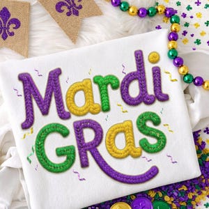 Könnte beinhalten: Weißes T-Shirt mit dem Schriftzug "Mardi Gras" in lila, gelben und grünen gestickten Buchstaben. Das Bild enthält dekorative Perlen, Münzen und Fleur-de-Lis-Banner, alles in festlichen Farben.