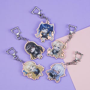 May include: Six anime-style character keyrings with silver cat-shaped clasps. Each keyring features a different character with unique hair and clothing, in shades of blue, black, and blonde. The keyrings are arranged on a purple and pink background.