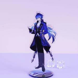 以下が含まれることがあります： 青い髪と長い青いコートを着たキャラクターのアクリルフィギュア。フィギュアは「FES 2026」の文字が入った透明な台座の上に立っています。キャラクターは白いアクセントが付いた黒い衣装を着ています。