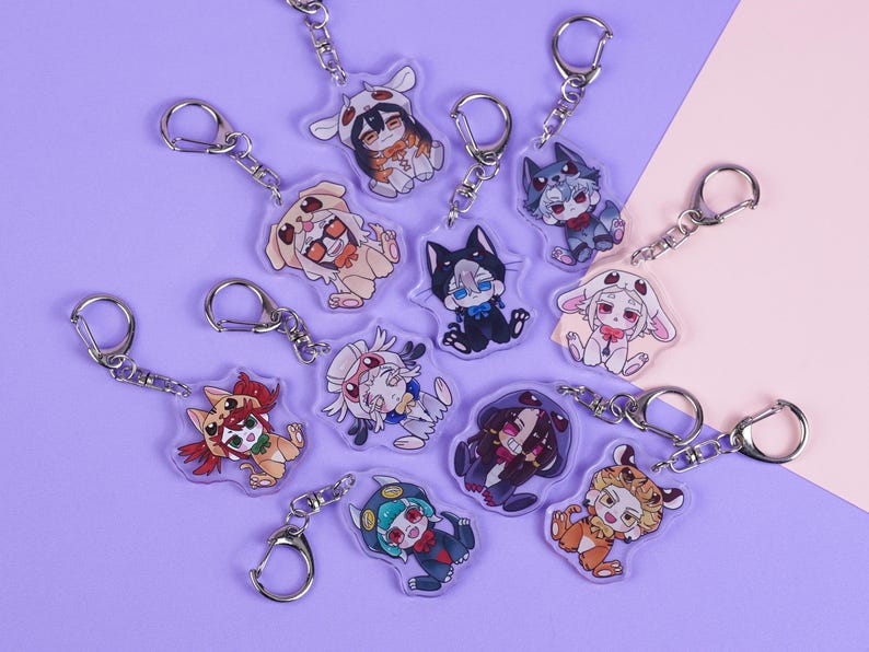 K&ouml;nnte beinhalten: Eine Sammlung von Acryl-Schl&uuml;sselanh&auml;ngern mit Anime-Charakteren in verschiedenen Tierkost&uuml;men. Jeder Schl&uuml;sselanh&auml;nger hat einen silbernen Verschluss. Die Charaktere sind in Braun-, Schwarz-, Wei&szlig;-, Orange- und Blaut&ouml;nen auf einem lila und rosa Hintergrund dargestellt.