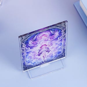 May include: A clear acrylic display featuring a vibrant illustration with purple and white hues. The artwork depicts a figure with flowing hair and ornate details, set against a celestial background. The display stands upright on a clear base.