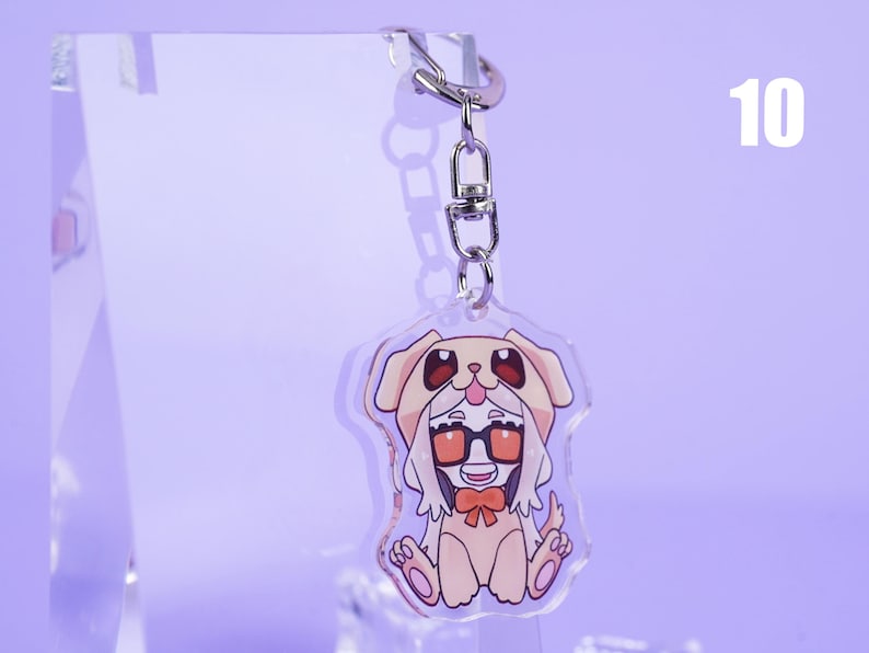 K&ouml;nnte beinhalten: Ein klarer Acryl-Schl&uuml;sselanh&auml;nger mit einer Cartoon-Figur in einem Hundekost&uuml;m. Die Figur tr&auml;gt eine Brille und eine Fliege. Der Schl&uuml;sselanh&auml;nger ist an einem silbernen Metallverschluss und -ring befestigt. Die Zahl 10 befindet sich im Hintergrund.