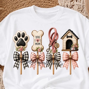 Può includere: Una t-shirt bianca con una stampa grafica composta da quattro elementi verticali: un'impronta di zampa nera, un osso con la scritta DOG MOM, un guinzaglio rosa e una cuccia. Ogni elemento è decorato con piccoli fiori rosa e un fiocco a motivi.