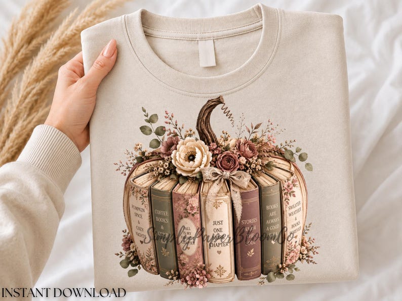 May include: A beige crewneck sweatshirt featuring a graphic of a pumpkin constructed from vertical books. The books are in shades of cream, sage green, and mauve, adorned with floral arrangements, a bow, and text on the spines.