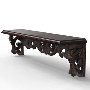 Op de afbeelding: Donkerbruin houten wandplank met sierlijke, gesneden bloemen- en bladerenontwerpen. De plank heeft een rechthoekige bovenkant en wordt ondersteund door twee decoratieve beugels. Het hout heeft een rijke, donkere afwerking en de gravures voegen elegantie toe.