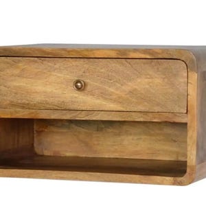 Könnte beinhalten: Ein Nachttisch aus Holz mit einer Schublade und einem offenen Regal. Der Nachttisch ist aus hellbraunem Holz mit sichtbarer Holzmaserung gefertigt. Die Schublade hat einen kleinen, runden, messingfarbenen Knopf. Die Kanten des Tisches sind abgerundet.