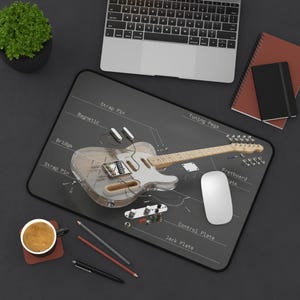 May include: A mouse mat featuring a transparent electric guitar with labeled components. The guitar is on a dark grey surface, with a laptop, coffee cup, and stationery nearby.