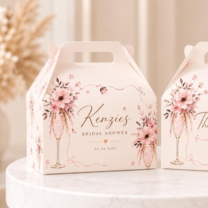May include: Two off-white gable boxes featuring a floral design with pink flowers and champagne flutes. The left box displays the text Kenzies BRIDAL SHOWER 01.24.2026, while the right box features the text Thank You! with small gold heart accents.