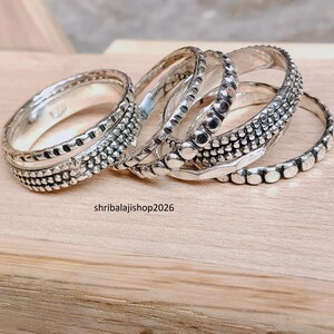 Könnte beinhalten: Eine Sammlung von Silberringen mit verschiedenen strukturierten Designs. Die Ringe weisen Muster aus Punkten, Linien und geometrischen Formen auf. Die Ringe werden auf einer hellbraunen Holzoberfläche präsentiert. Der Text "shribalajishop2026" ist sichtbar.