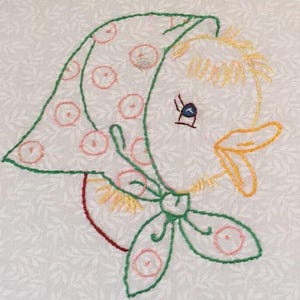 May include: Embroidered image of a cartoon duck wearing a green scarf with pink circles and a matching bonnet. The duck has yellow hair, a yellow beak, and a blue eye. The background is white with a subtle leaf pattern.