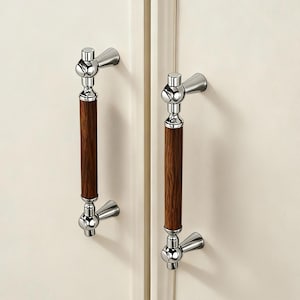 May include: Two cabinet door pulls with a polished chrome finish and dark brown wooden handles. The pulls are mounted on a cream-coloured cabinet door. The design features a classic, elegant aesthetic.
