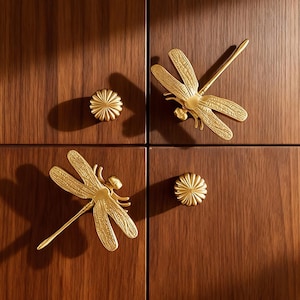 Peut inclure: Quatre portes d'armoires avec quincaillerie dorée. Deux poignées en forme de libellule et deux boutons ronds en forme de fleur sont montés sur les portes en bois brun foncé. Les poignées libellule ont des ailes détaillées et un corps long et fin.