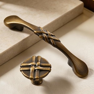 Può includere: Un set di ferramenta per mobili in bronzo antico, tra cui una maniglia lunga e un pomello rotondo. La maniglia presenta un design intrecciato al centro ed entrambe le parti hanno un aspetto classico e invecchiato. Ideale per il restauro di mobili.