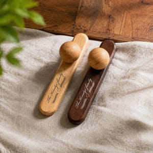 May include: Two wooden door stops, one light-toned and one dark-toned, each featuring a spherical handle at the top. Both pieces are engraved with the text The Kenedys' family, a small heart icon, and a decorative vine pattern along the centre.