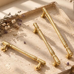 May include: Three gold-toned metal cabinet pulls with a smooth, cylindrical design and flared ends. Each handle features the engraved text "The Hendy family" along the centre bar. The pulls are arranged diagonally, showcasing a polished finish.