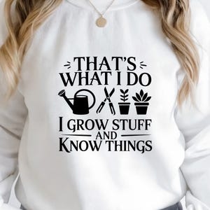 Puede incluir: Una sudadera blanca de manga larga con texto negro que dice THAT'S WHAT I DO I GROW STUFF AND KNOW THINGS. El dise&ntilde;o incluye iconos gr&aacute;ficos negros de una regadera, tijeras de podar y dos plantas en maceta centrados en el pecho.