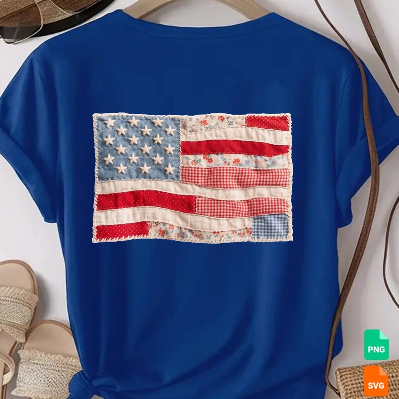 May include: A blue t-shirt featuring a patchwork American flag design. The flag includes a denim blue field with white stars, and red and white striped sections with floral and gingham patterns. The shirt has short sleeves.