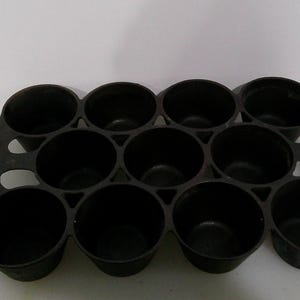 May include: A black muffin tin with twelve round cavities. The tin is made of a dark material and is designed to hold individual muffins or cupcakes. The cavities are evenly spaced and appear to be of a standard size.