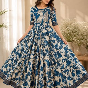 May include: A floor-length dress featuring a cream base with a blue floral print. The bodice displays a stylized peacock graphic. The garment has a round neckline, three-quarter length sleeves, and a wide, flared skirt with a dark blue border.