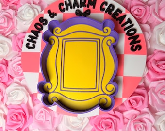 May include: A yellow, purple, and gold decorative frame with the text "Chaos & Charm Creations" on a pink and white checkered background. The frame is surrounded by pink and white roses.