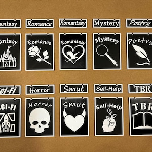 May include: Black and white genre-themed decorative signs. Each sign features a title like "Fantasy," "Romance," or "Mystery," along with a corresponding graphic. The signs are designed for book lovers and readers.