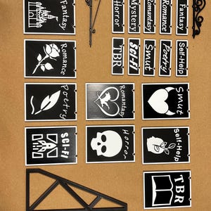 May include: Black and white signs with various genre labels, including "Fantasy," "Romance," "Horror," and "Sci-Fi." The signs are designed to hang from a decorative bracket, perfect for a bookstore or library.