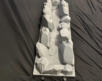 May include: A grey diorama base with a rocky canyon design. The canyon walls are made of large, angular grey rocks. The base has two metal supports on the bottom. The background is a black fabric.