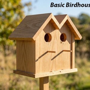 Könnte beinhalten: Ein Vogelhaus aus Holz mit dem Text "Basic Birdhouse" oben. Das Vogelhaus hat zwei kreisförmige Eingangsöffnungen und zwei kleine Sitzstangen. Es besteht aus hellem Holz und ist auf einem Holzpfosten montiert.