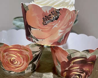 Puede incluir: Tres cápsulas para cupcakes con un patrón floral. Las cápsulas son de color rosa, marrón y verde con detalles dorados. La cápsula superior tiene un cupcake blanco con glaseado.