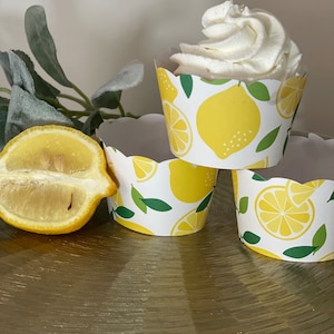May include: Three yellow and white cupcake liners with a lemon print. The liners are stacked on top of each other. The top liner has a white cupcake with white frosting.