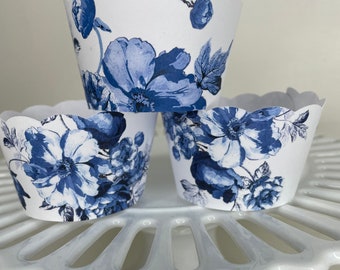 May include: Three white cupcake liners with a blue floral pattern. The liners are on a white cake stand.