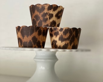 May include: Three brown and tan leopard print cupcake liners on a white cake stand.